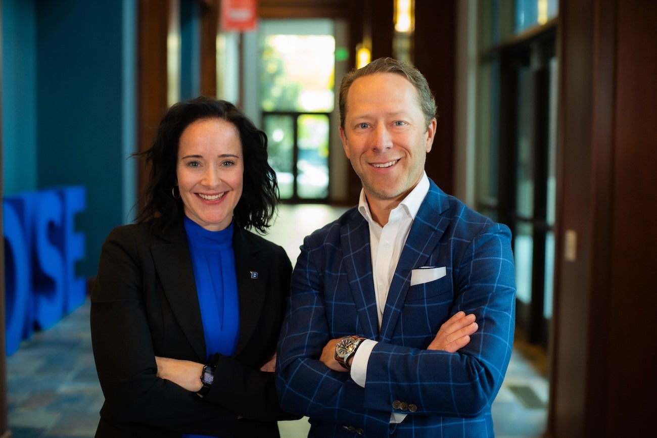 Two persons pose in suits with their arms crossed