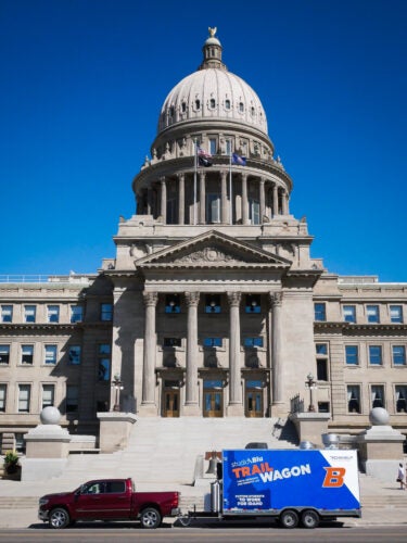 A red truck tows the bright blue TRAIL Wagon trailer in front of the Idaho capitol building.