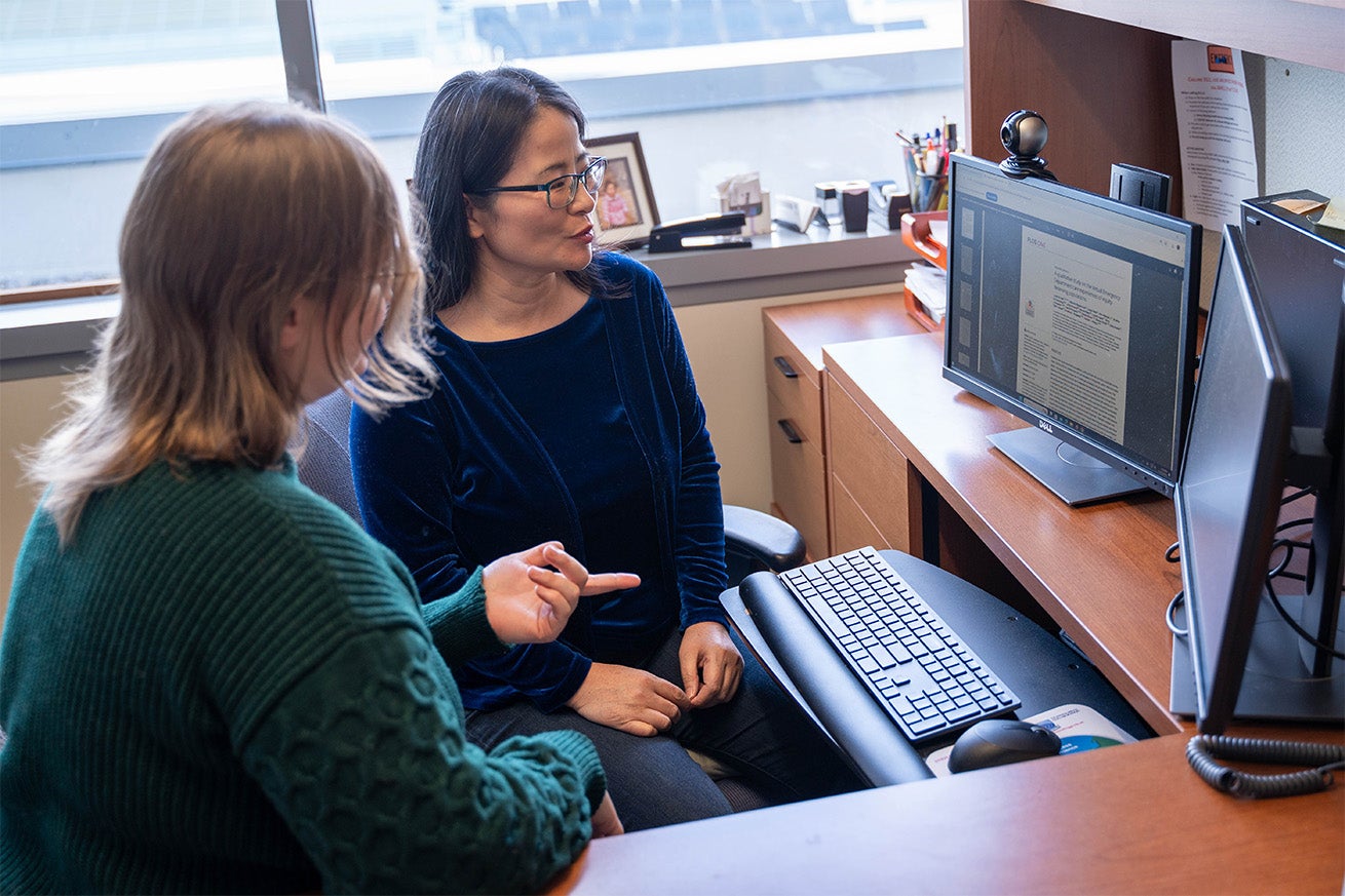 Lucy Zhao looks at a computer screen and talks to a student pointing at something.