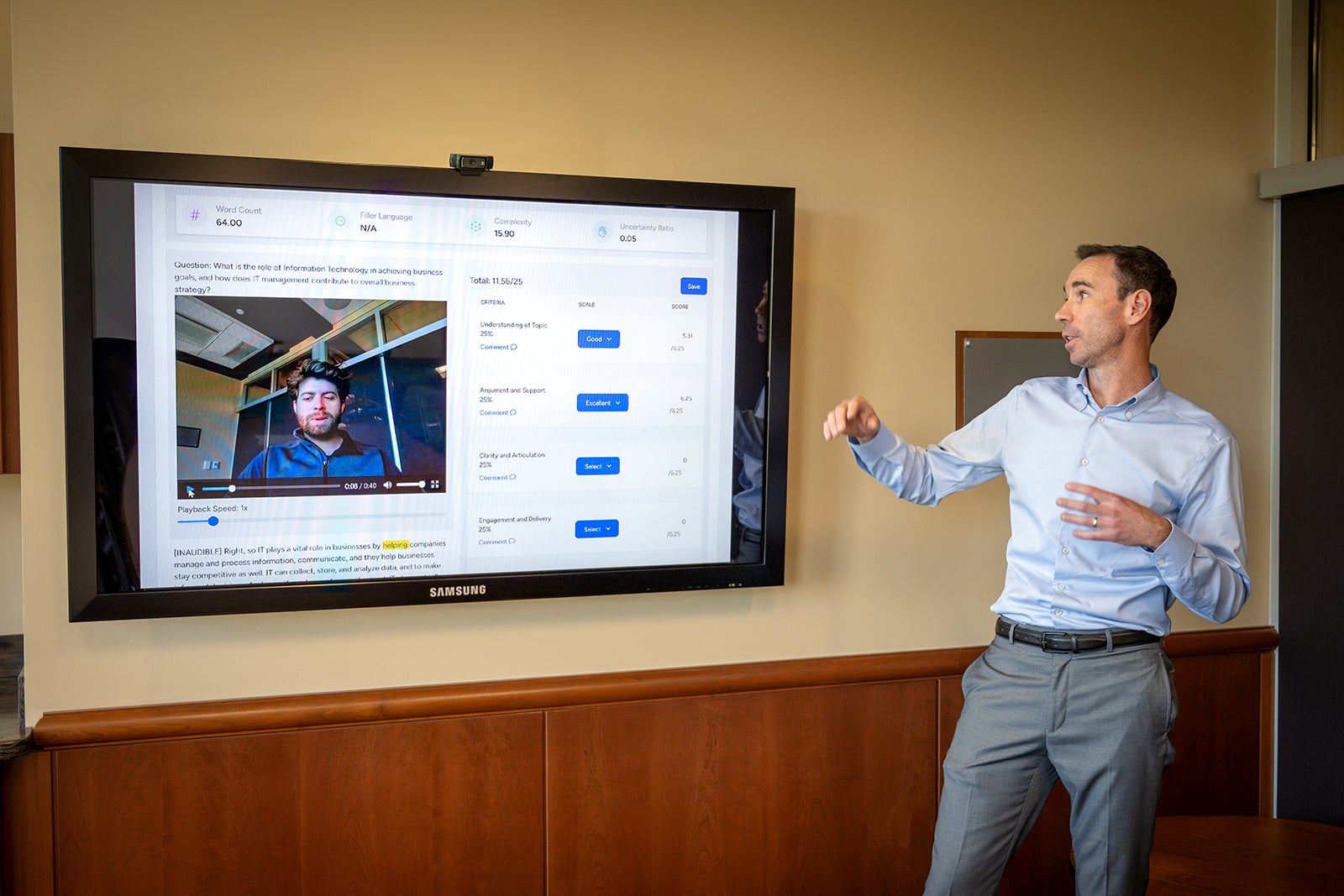 A man stands in front of a large television screen with a software on the display.