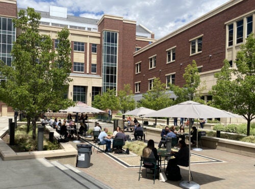 Conference participants have lunch on a sunny day at the tables in the ICCU square.