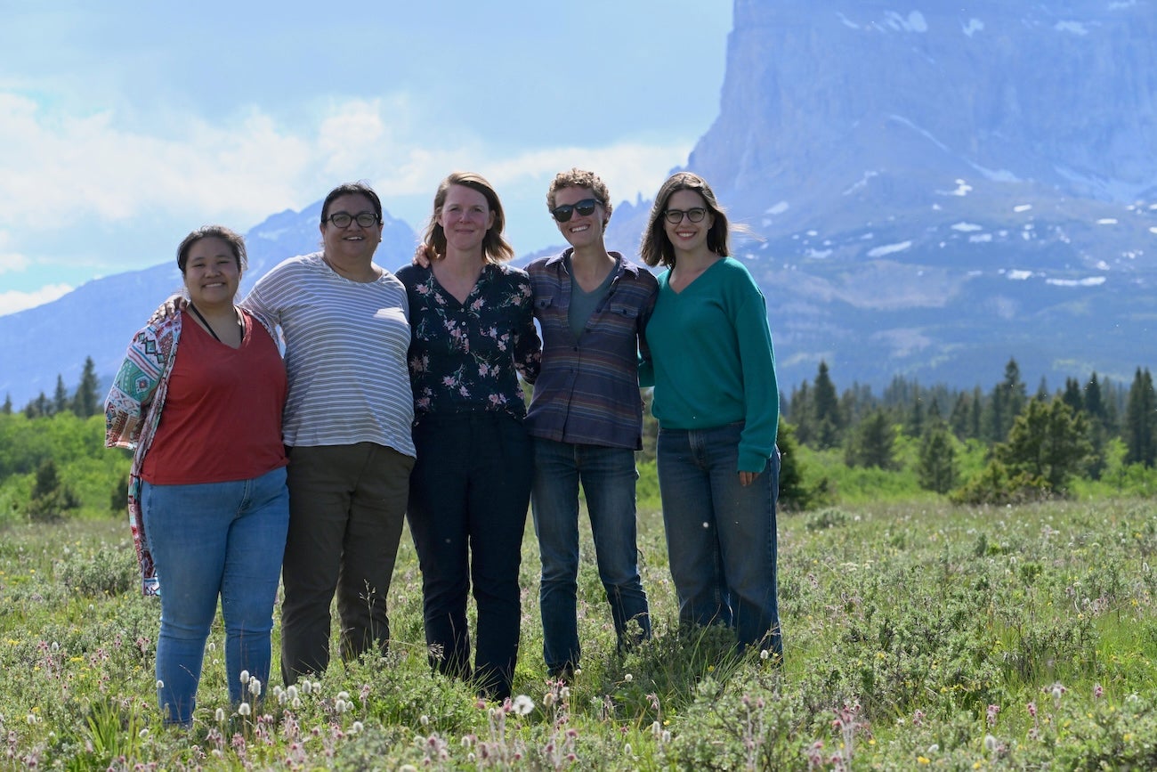 Fiver persons pose in front of a mountain backdrop