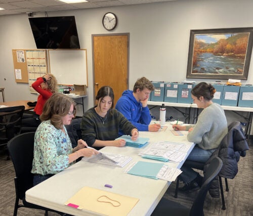 A group of people sitting at a table look intently at paperwork.