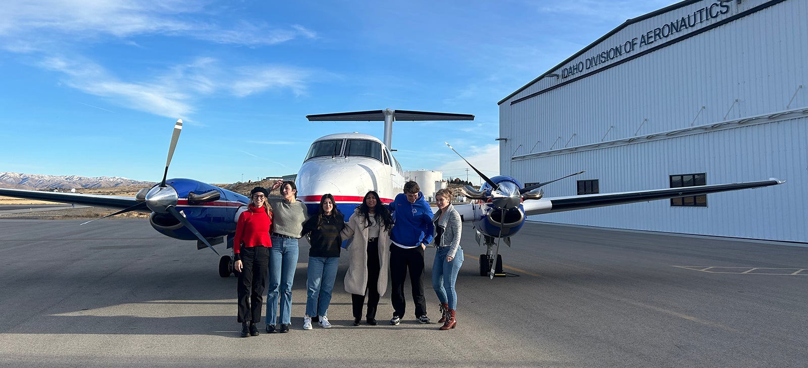 A group of six accounting students stand on the tarmac in front of a small private plane