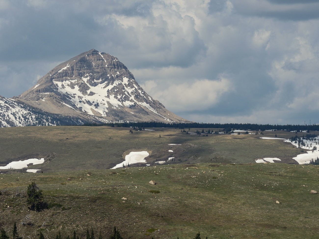 A mountain and pockets of snow on a meadow