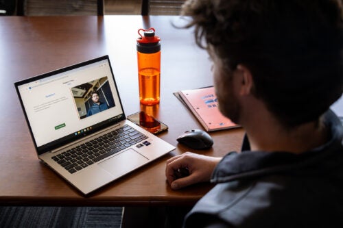 A young man looks at a laptop that's recording him with a question on the screen.