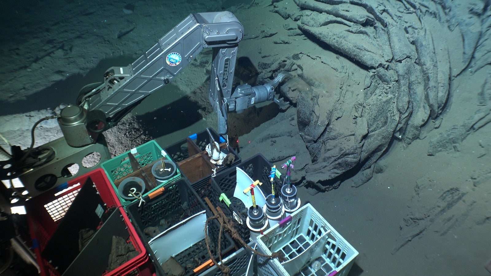 view from insidea. submersible. A long metal arm collects rock samples and places them into grid of baskets