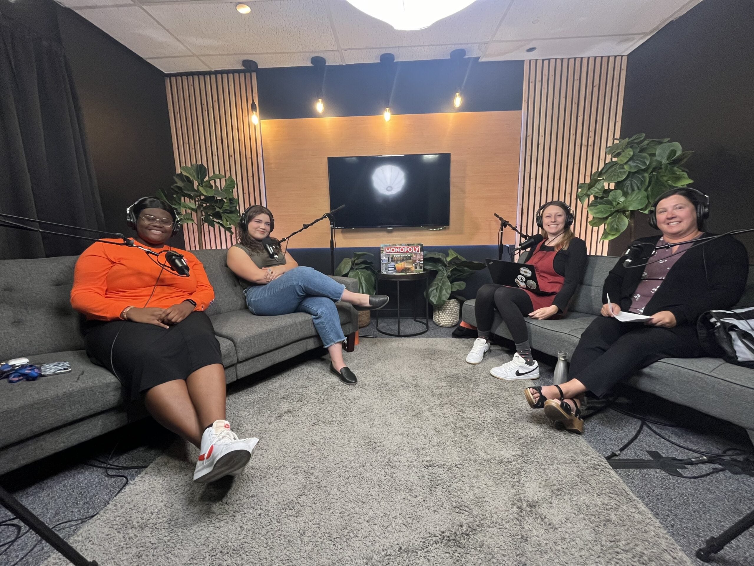 Students and faculty member with podcast host sit on couches with recording equipment at a podcast studio. They smile for a picture. 