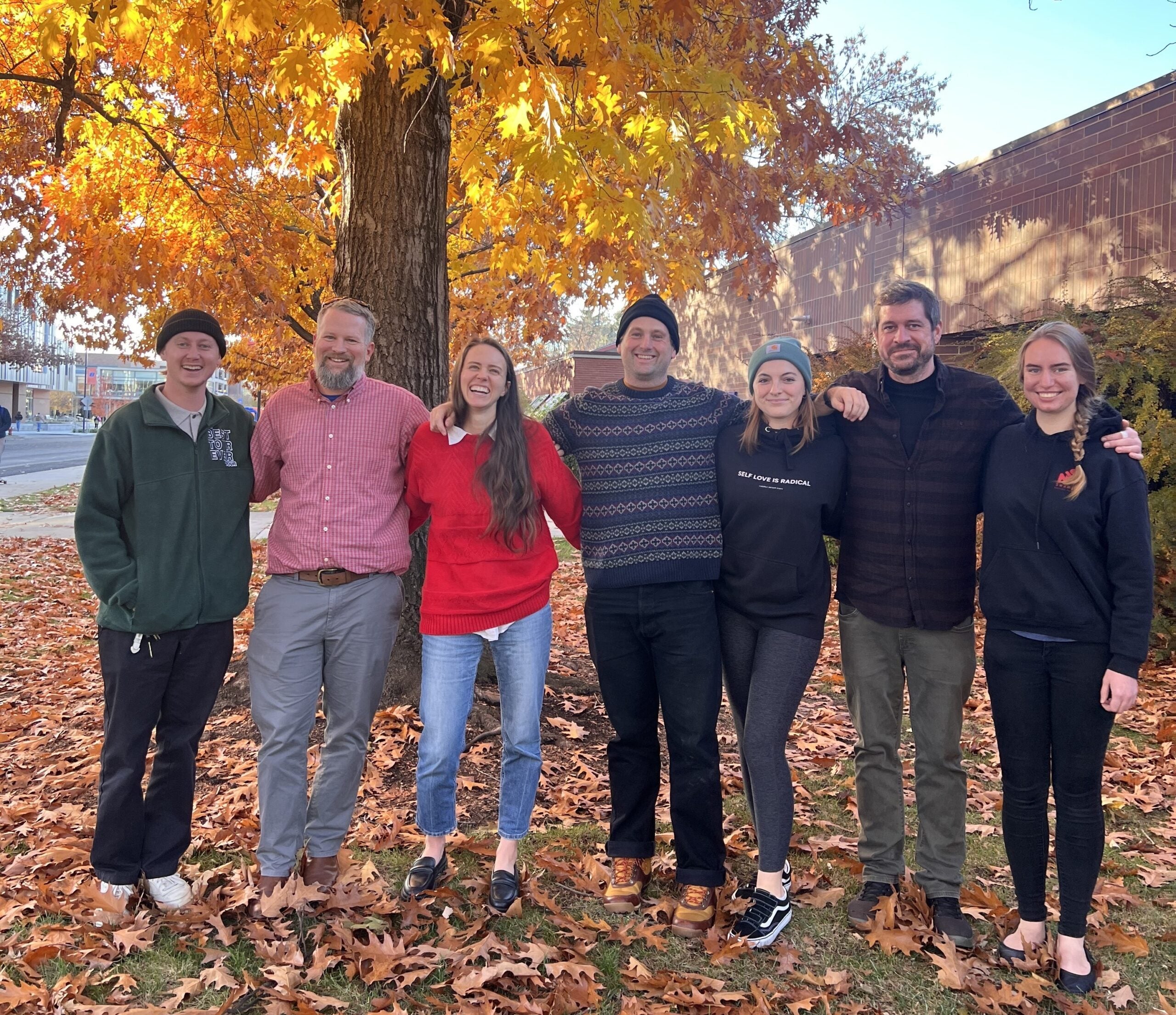 Seven staff and faculty members of Boise State University pose for a photo in front of a tree during autumn. 