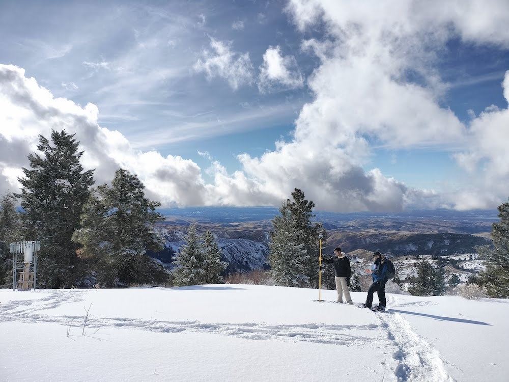 Persons use survey equipment in a snowy mountain range