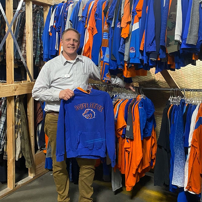 Scott Curtis surrounded by Boise State clothing holds a Boise State sweatshirt