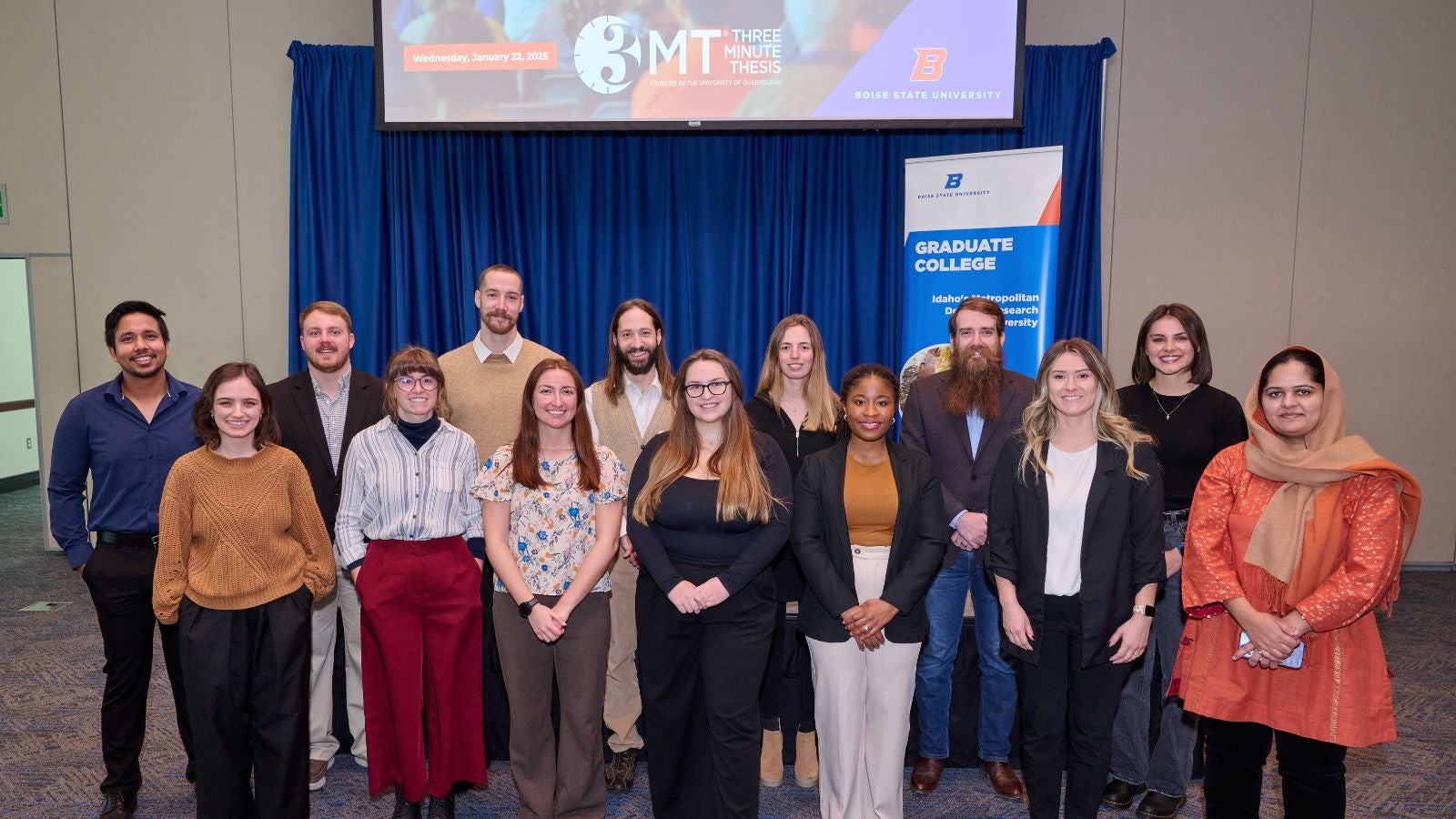 A group of persons pose in front of a Three Minute Thesis digital screen