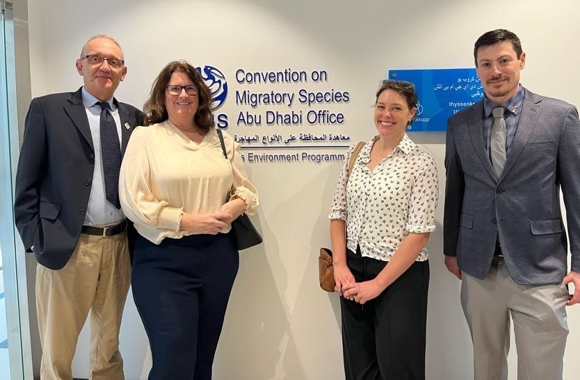 Four people pose in front of a sign that says "Conservation of Migratory Species Abu Dhabi Office".