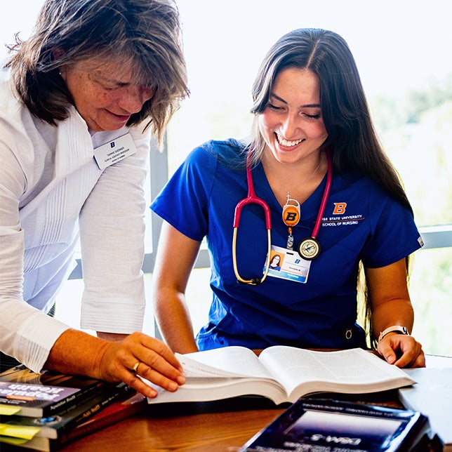 Nursing student smiles as a professor leans over a textbook and shows her something.