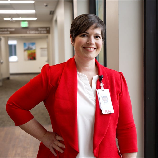 Lauren Smith wears a red blazer and stands smiling in a hallway.