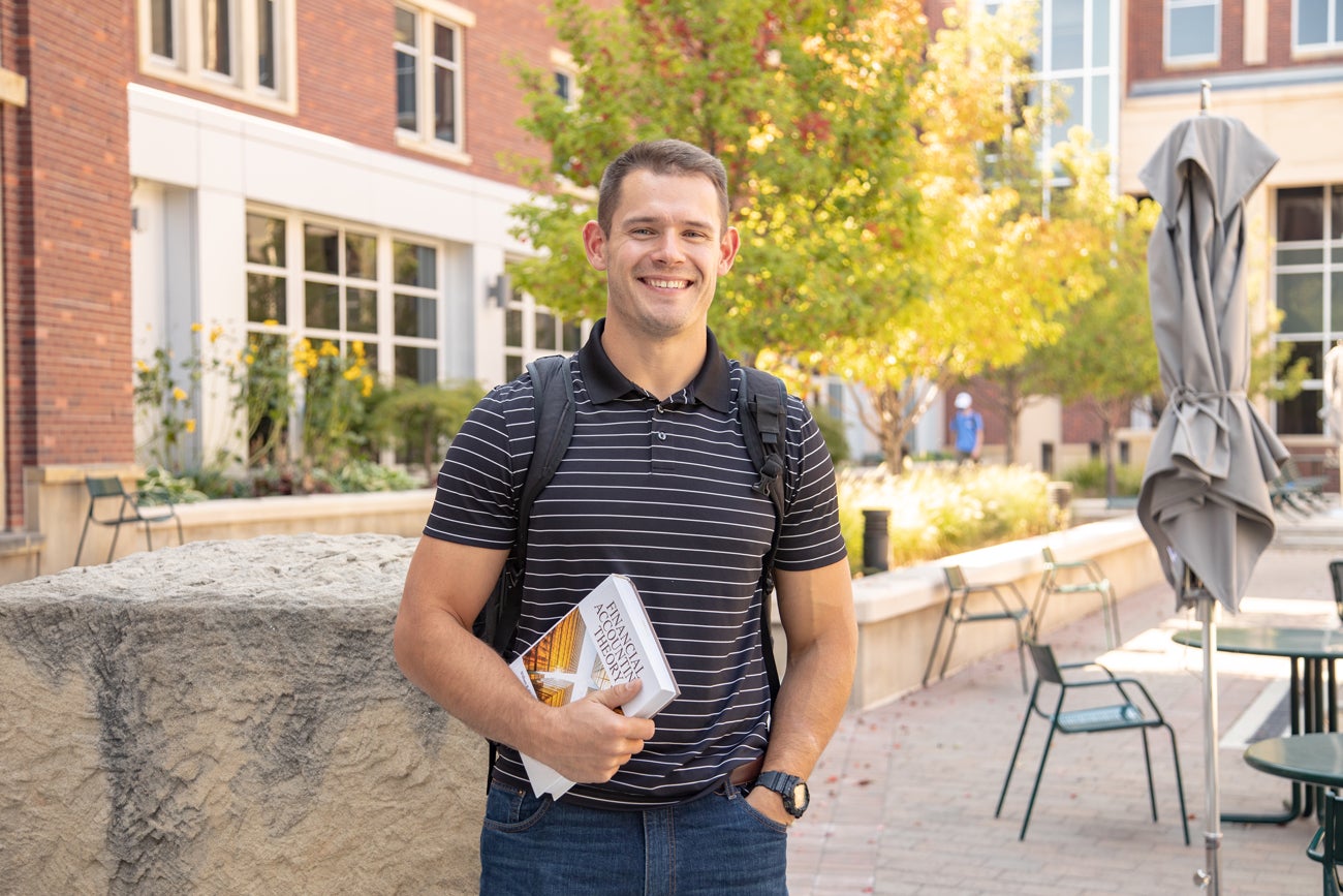 Mason Hampton stands outside of a brick building and holds a textbook.