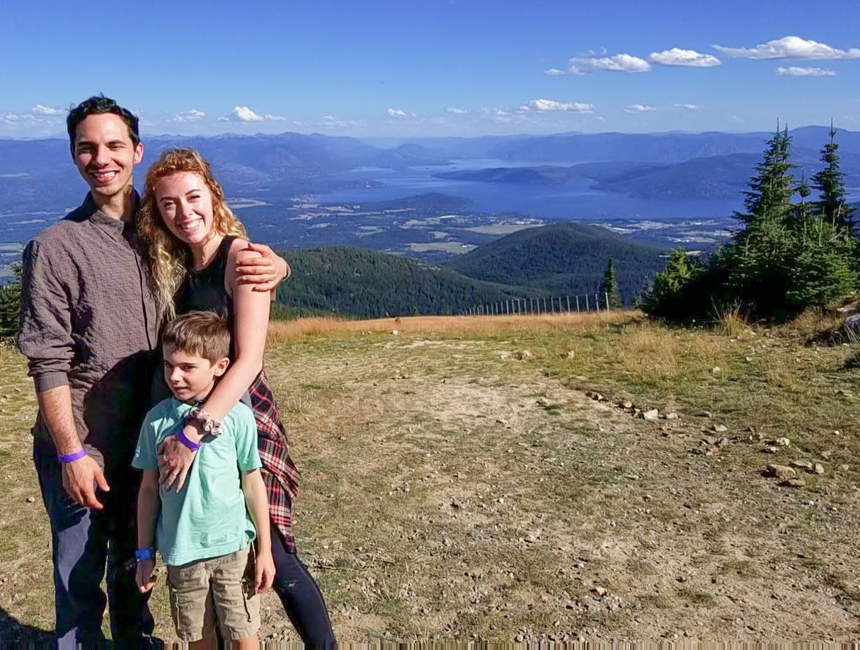 Meghan Howk, her husband, and son stand together with a mountainous view behind them.