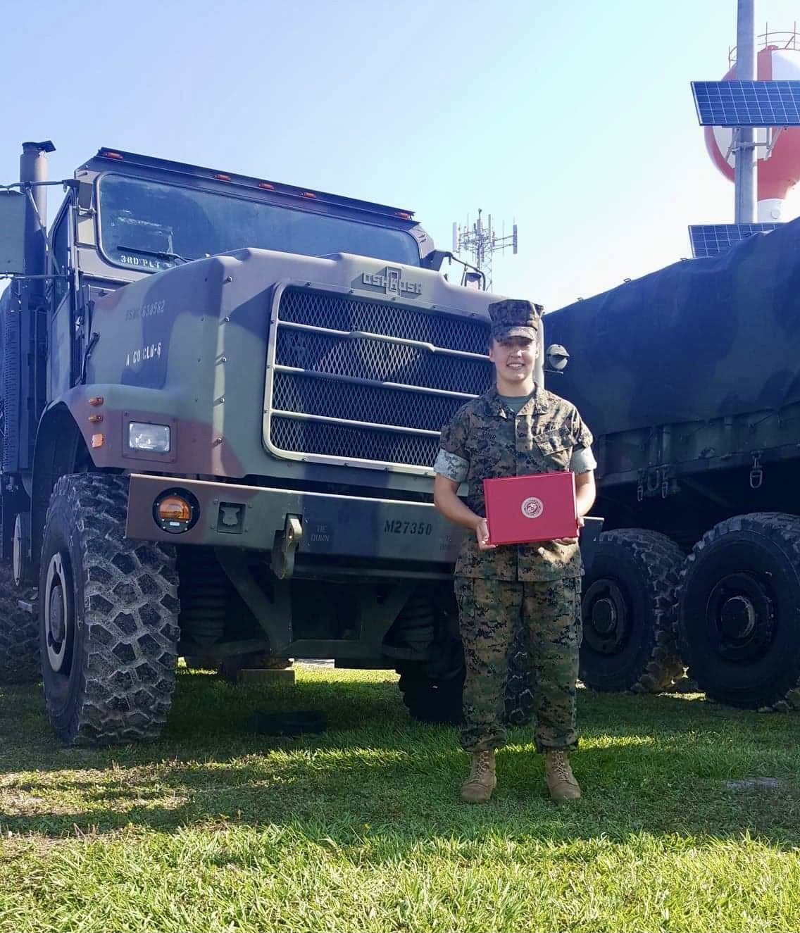 Brieann Jones poses in front of a military vehicle and holds an award.