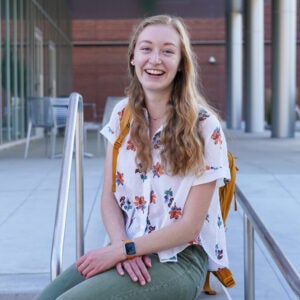 Clara Adams sits on outside steps, smiling into the camera.