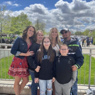 A family stands together outdoors and smiles.