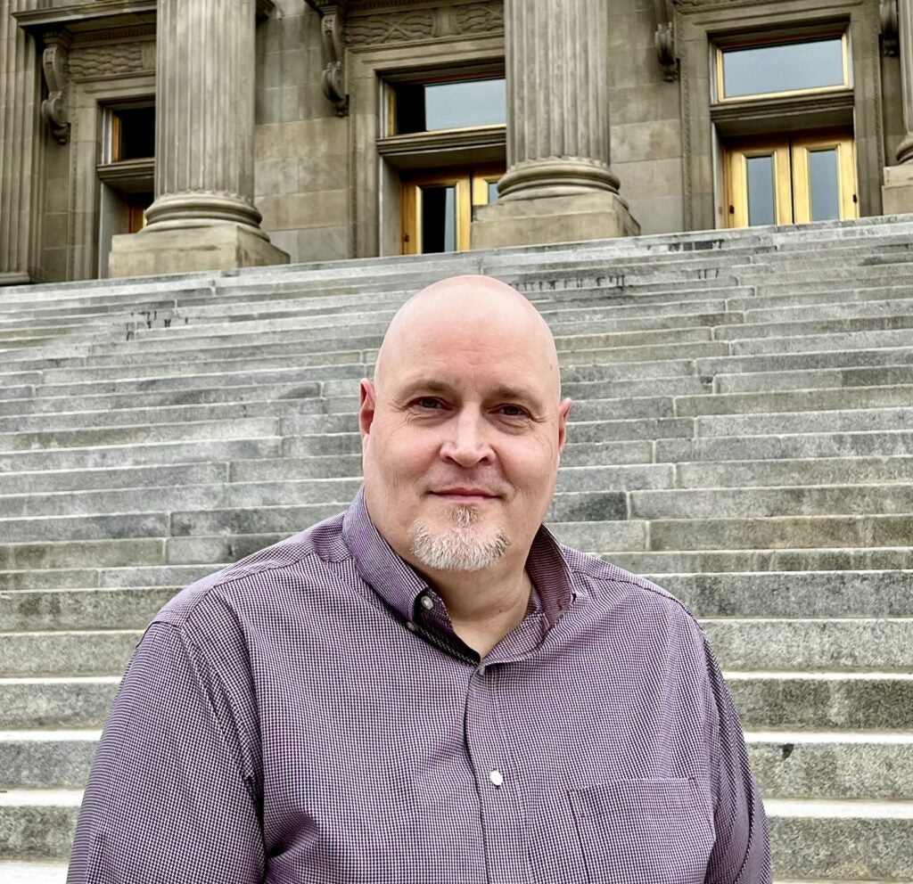 Paul Tucker stands and smiles in front of the Idaho capitol steps.