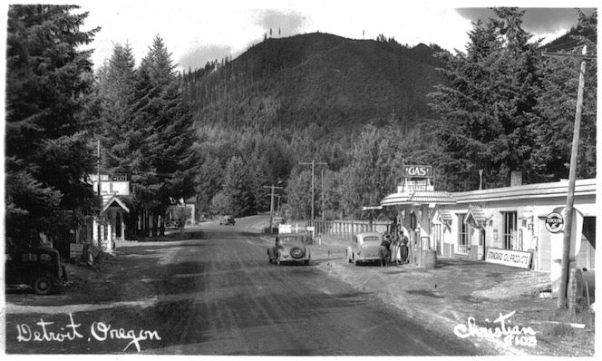 Small town, dirt road, gas station, cars, mountains, trees.