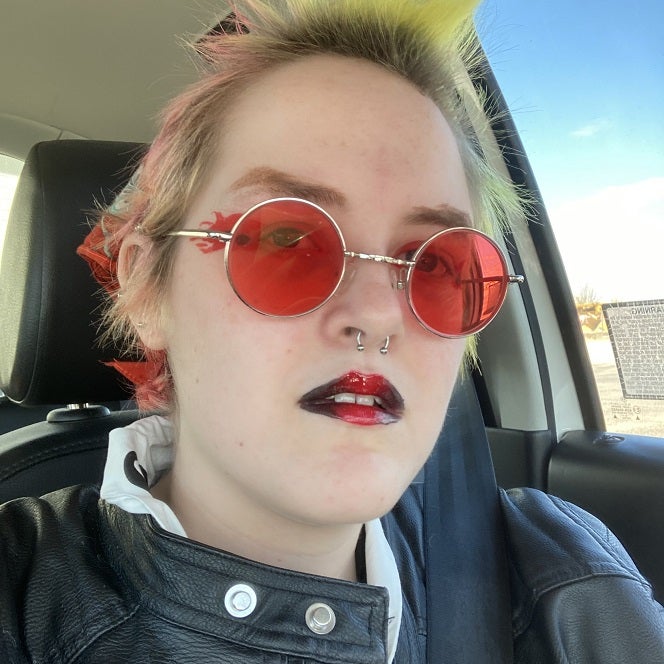Finch Johnson, A pale person with fading pink and yellow dyed hair wearing a leather jacket and red glasses.