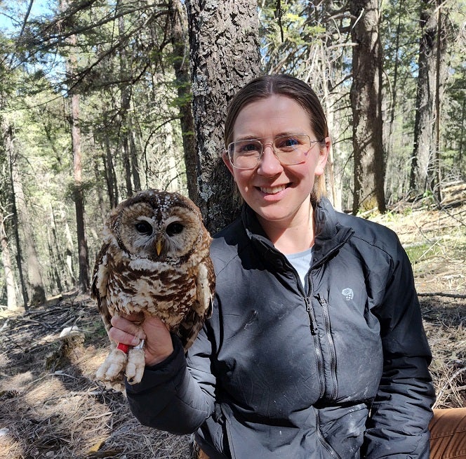 Michaela Gustafson smiling and holding a spotted owl in the forest