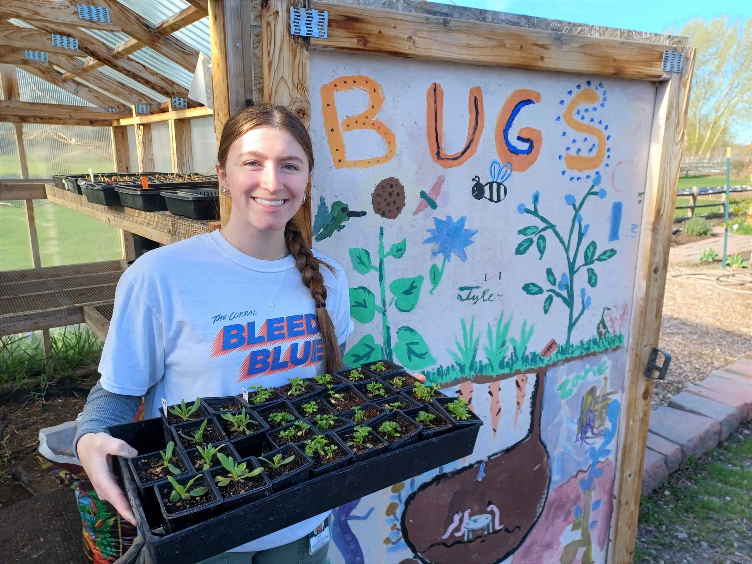 Service-Learning student holding a tray of seedling at a community garden.