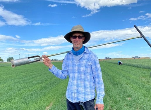 A man standing in a farmer's field with a soil core tool.