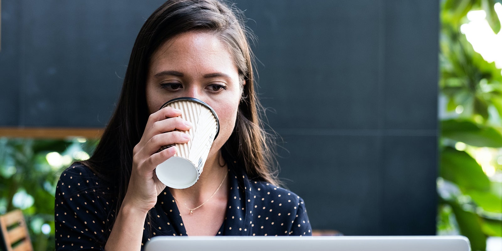 A woman drinking coffee while working at her laptop