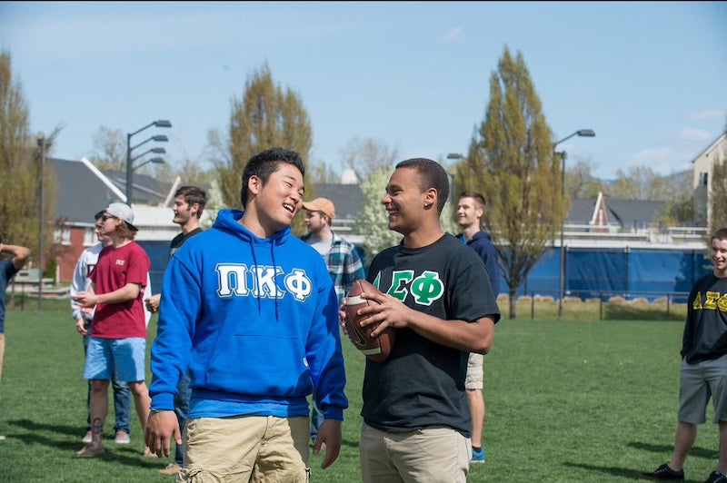 Two students chat on sports field. One holds a football