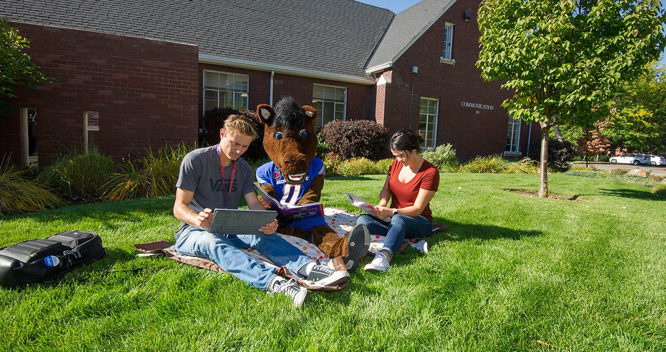 Students sit outside the Communication building with Buster Bronco