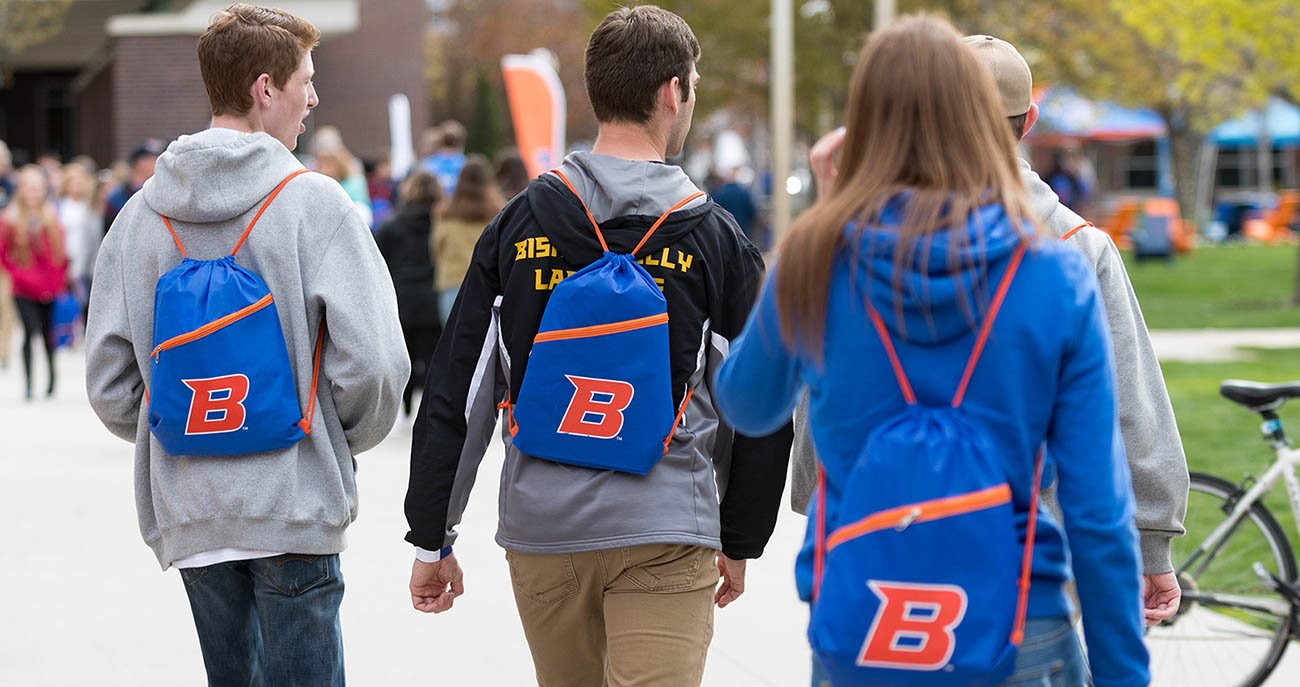 Three students walking through campus wearing Boise State branded backpacks.