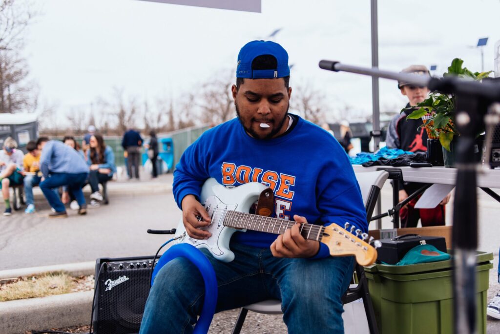 Man wearing blue Boise State sweater strums electric guitar while sitting at Treefort.