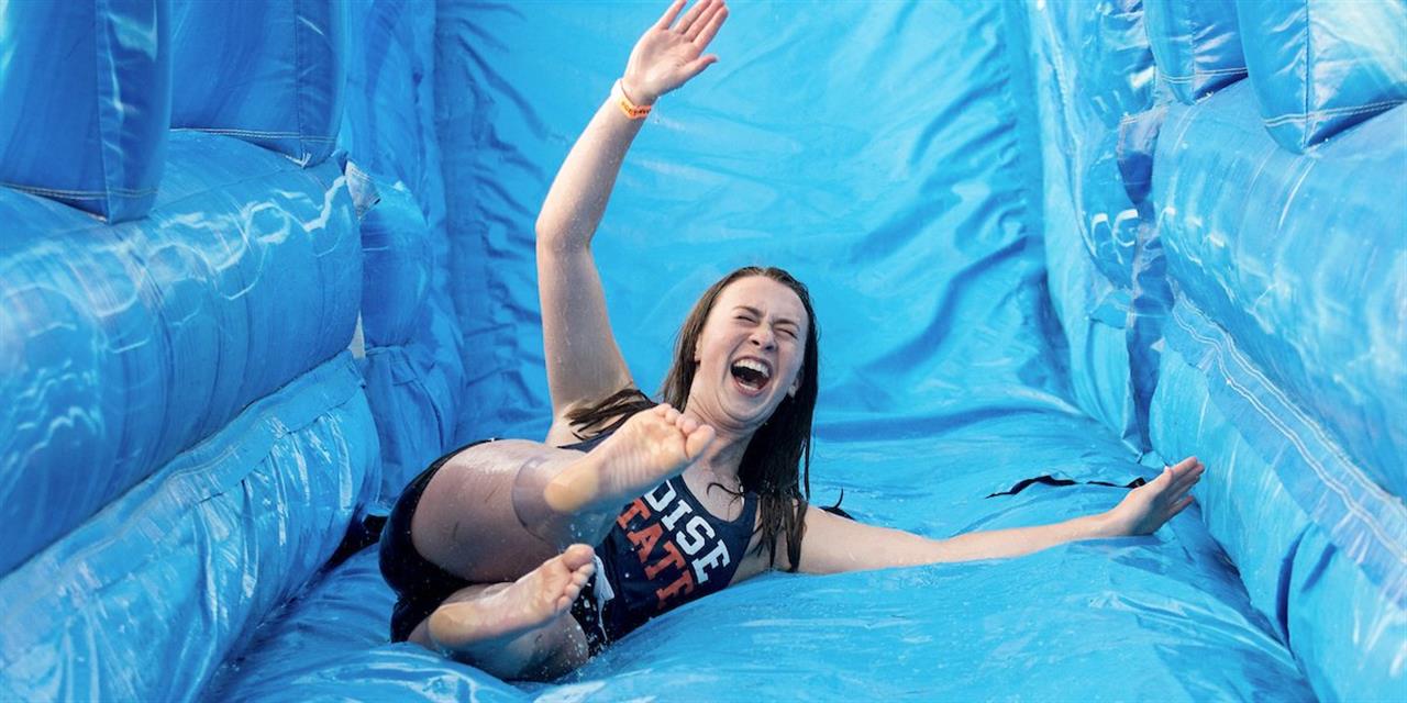 Student laughing sliding down an inflatable water slide.
