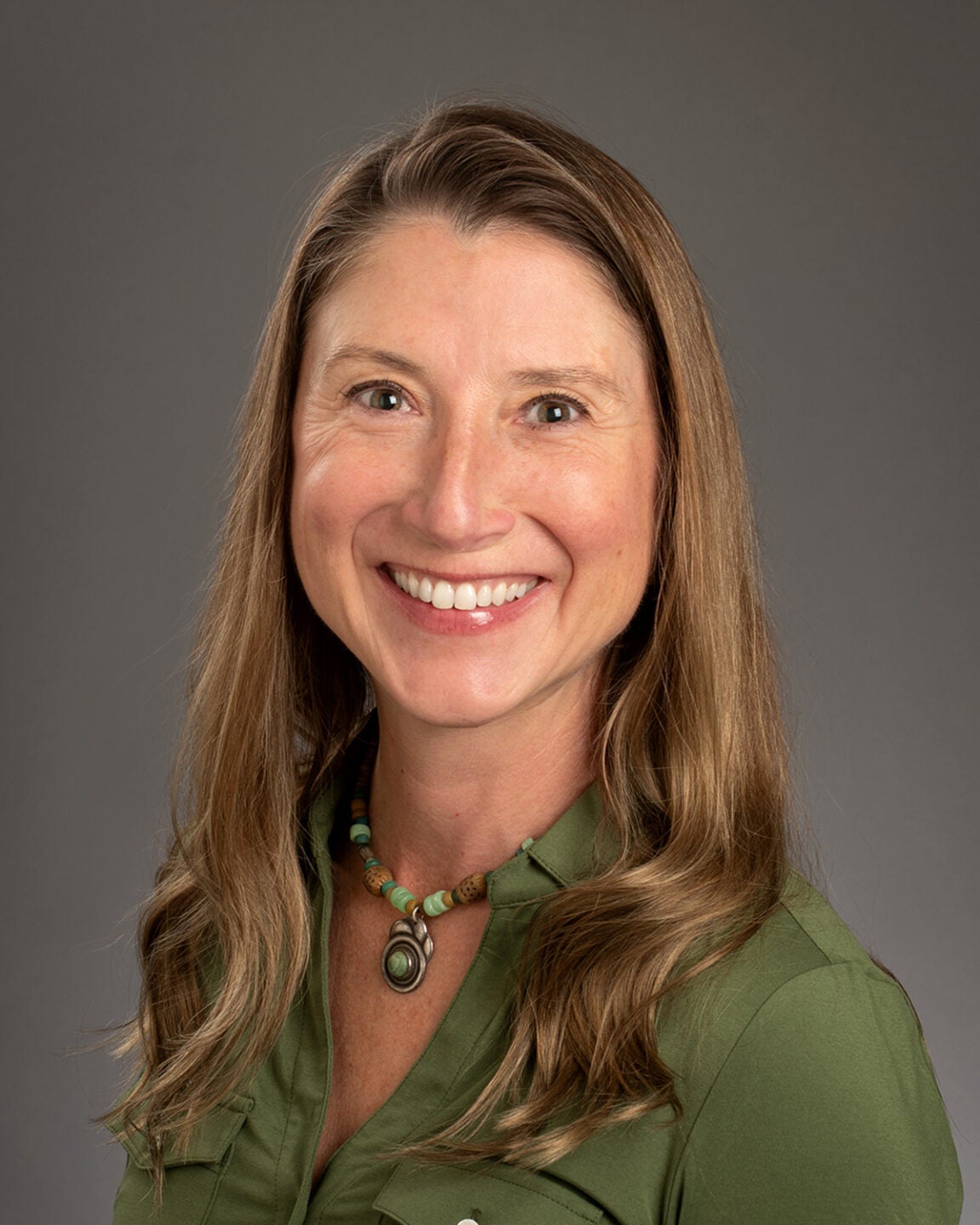 A portrait of a blonde woman smiling, with a Boise State hat.