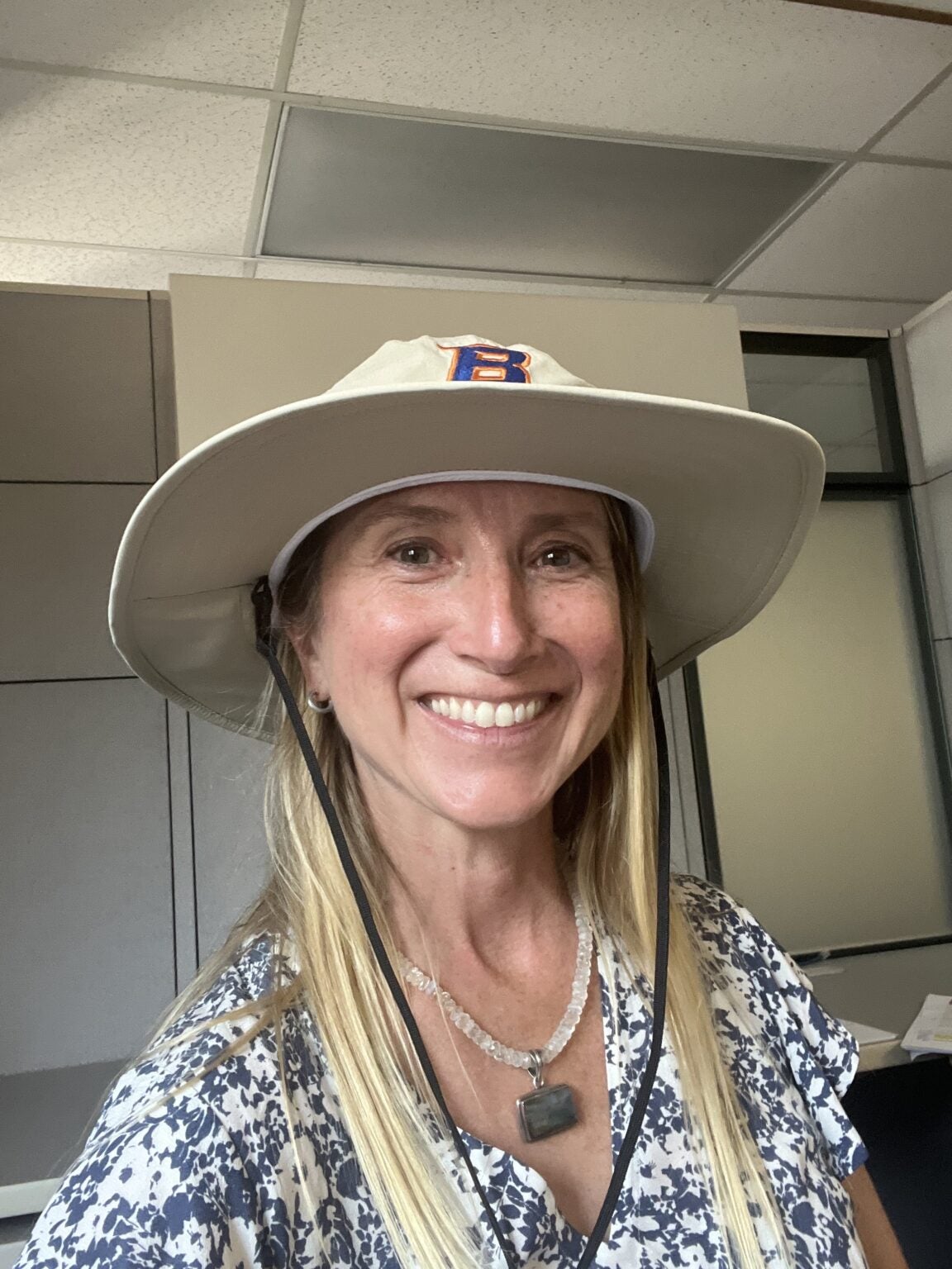 A portrait of a blonde woman smiling, with a Boise State hat.