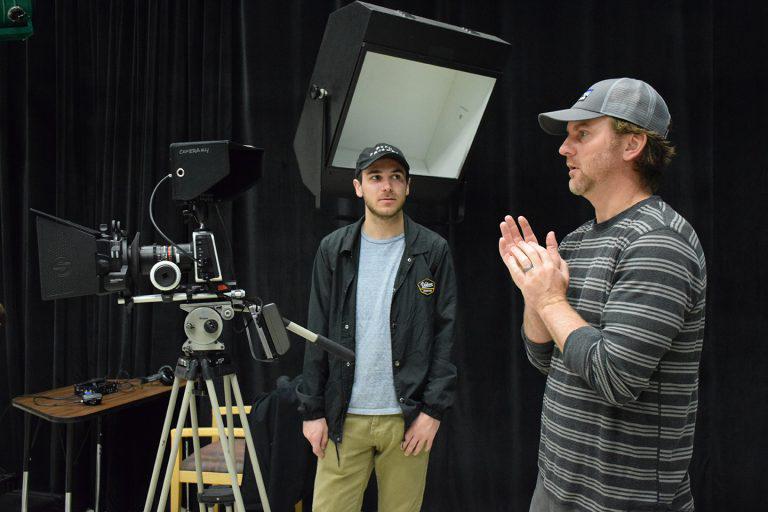 A film professor speaks with a student in front of a camera