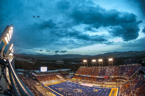 Bronco stadium at dusk with band on field and two jets overhead