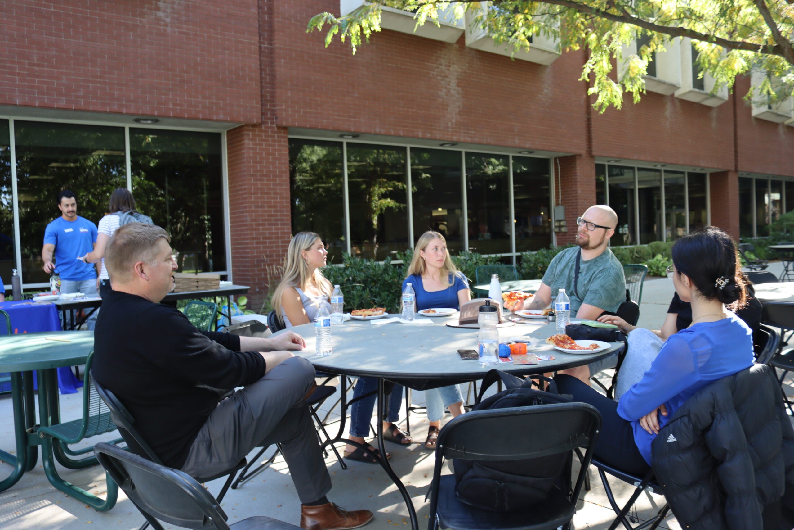 students and faculty sitting around a table talking and eating pizza