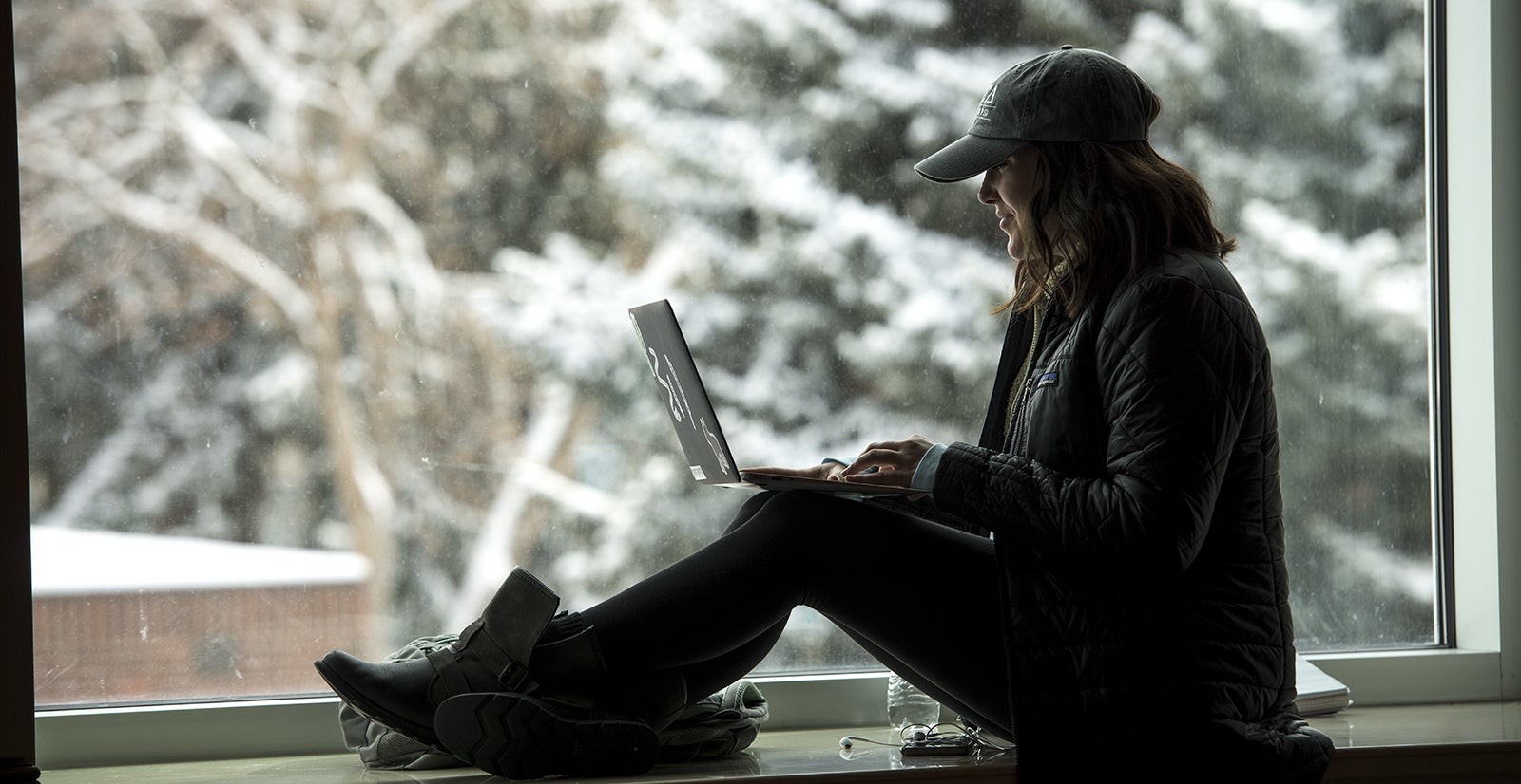 student working on laptop while sitting by a window with a snowy scene